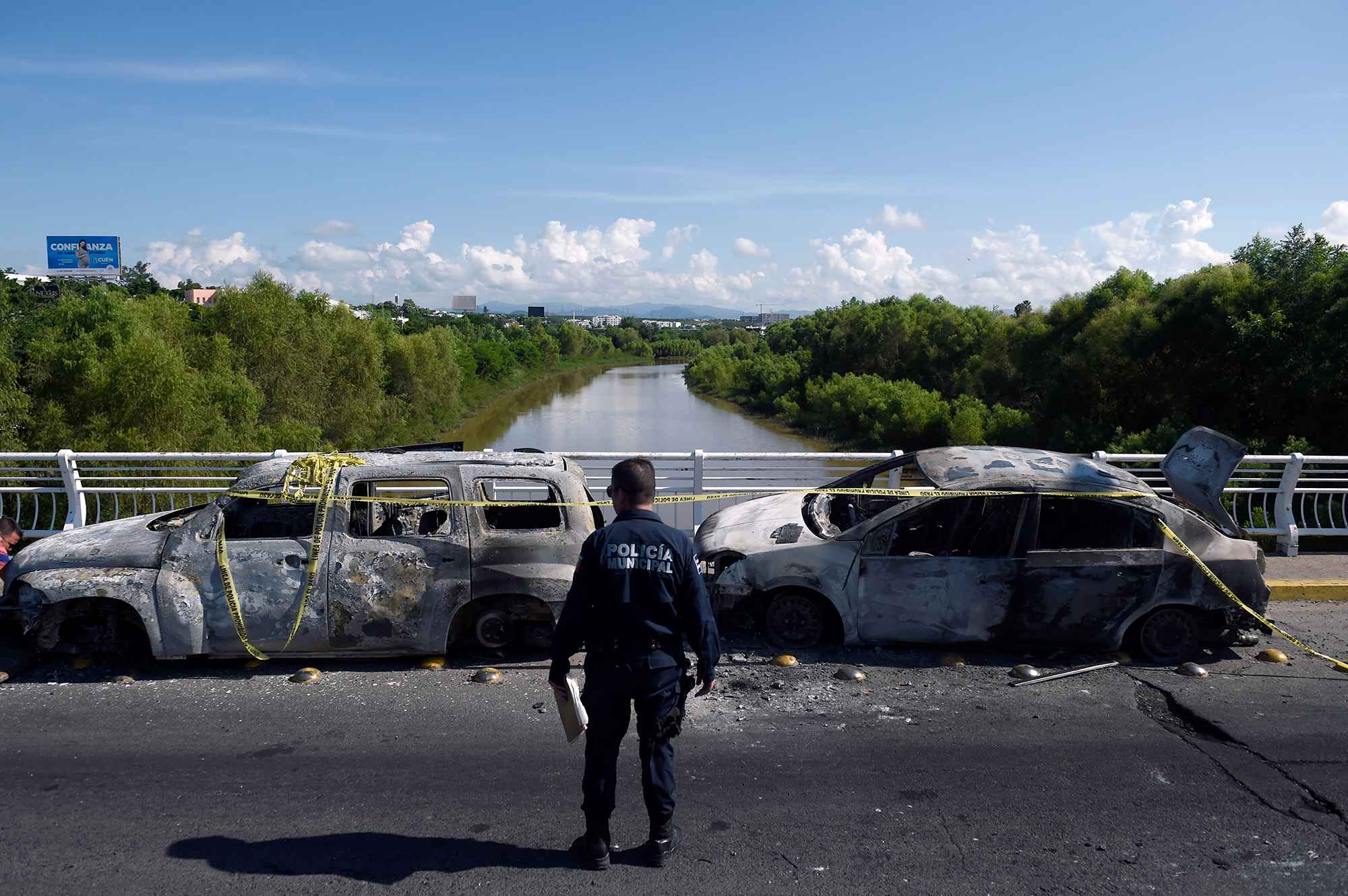 La narcoviolencia somete a México. Un policía se encuentra al lado de vehículos quemados después de que hombres fuertemente armados libraron una batalla total contra las fuerzas de seguridad mexicanas en Culiacán, estado de Sinaloa, el 18 de octubre de 2019. El presidente de México, Andrés López Obrador, enfrentó una tormenta de críticas luego de que sus fuerzas de seguridad confirmaran el arresto del hijo del capo Joaquín "El Chapo" Guzmán, y luego notificaran su liberación tras un ataque frontal en Culiacán perpetrado por el crimen organizado. Según la Secretaría de Seguridad Pública de Sinaloa, en el ataque armado murieron 14 personas. Foto por Alfred Estrella/AFP.