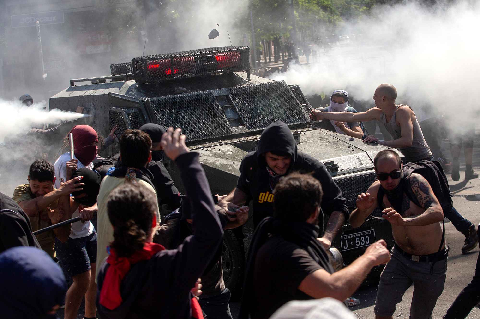 Estallido social en Chile. El viernes 18 de octubre, el aumento en casi 4 centavos de dólar en la tarifa del metro provocaron una oleada de protestas en Chile que han provocado 18 muertos, cinco de ellos por acción de agentes del estado, en medio de crecientes denuncias de abuso policial y militar. Las maifestaciones se han convertido ahora en una suerte de catarsis nacional sin final a la vista y los chilenos también protestan por las bajas pensiones, precariedad en salud y educación, una desigualdad crónica o la poca empatía de la clase política. En la imagen, manifestantes se enfrentan con un vehículo de la policía antidisturbios el 20 de octubre. Foto por Claudio Reyes /AFP.