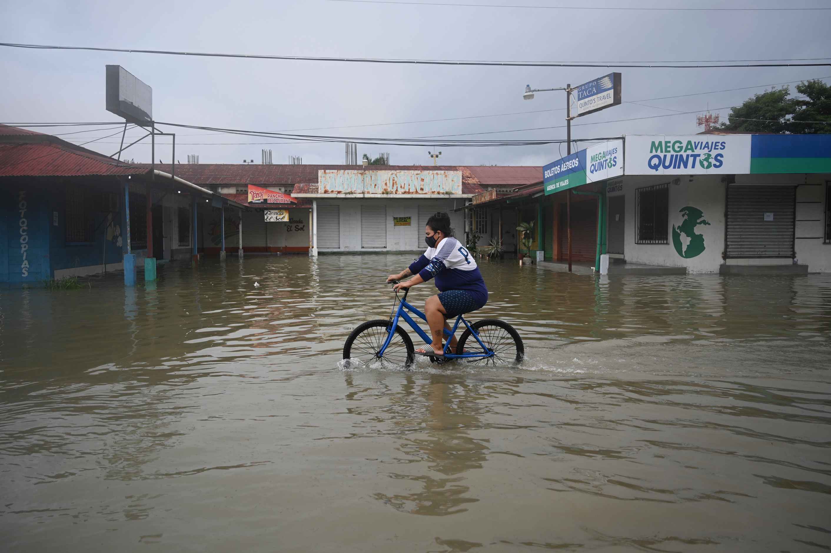 A woman rides a bike in a flooded street due to the heavy rains caused by Hurricane Eta, now degraded to a tropical storm, in Puerto Barrios, Izabal 310 km north Guatemala City on November 5, 2020. - At least four people, including two children, died in landslides as tropical storm Eta swept through Guatemala, civil protection officials said Thursday. The death toll from hurricane Eta rose to at least 12 Thursday as it spun itself out into a tropical depression in Central America, while rising floodwaters and a wake of destruction in Nicaragua, Honduras and Guatemala left thousands without shelter and at risk of landslides. (Photo by Johan ORDONEZ / AFP)