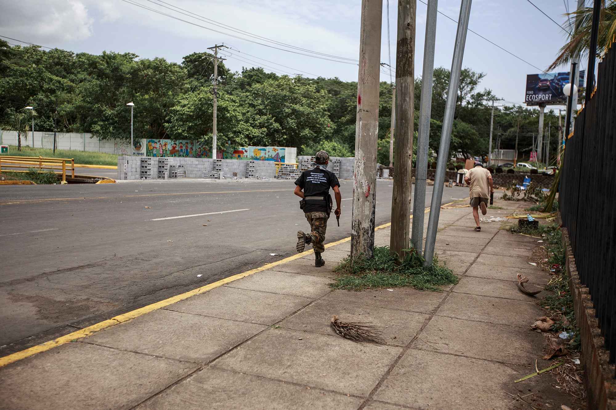 Two armed students, one carrying a 9 millimeter pistol and the other an improvised mortar, run to the university's northwest entry point after police attack one of the barricades. One of the barricade's guards, Isaías Emilio Puerto, 20, died during the attack. June 30, 2018.