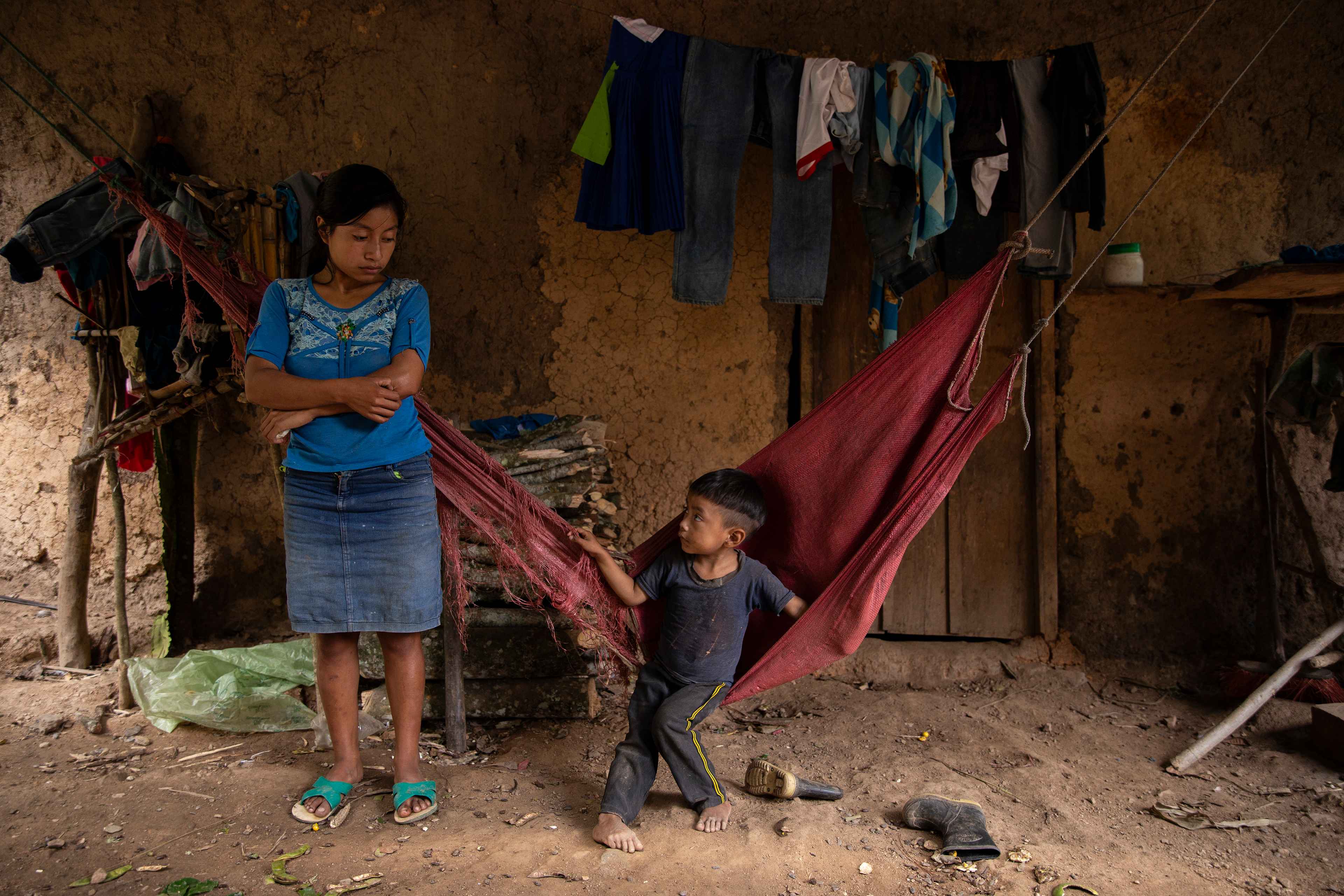 Herminia Gutiérrez y su hijo viven en la misma casa donde murieron Adalicia, de cinco años, y María Isabel, de seis meses, en septiembre de 2021. Sus hermanitas son parte de la tasa de mortalidad de 18 menores que la comunidad ha registrado desde el año 2013 a causa de la desnutrición. La vivienda está construida en medio de una ladera, sin acceso a agua potable, rodeada de cafetales, patos, gallinas y algunos perros desnutridos que duermen sobre el patio de tierra. Herminia ahora tiene 20 años, y sólo alcanzó una altura de 1.25 metros. Creció bajo pobreza extrema y parece haber perdido el horizonte y la noción del tiempo. Según lo cuenta, la niña más grande se cayó en el polvo; que un gusano se le metió en el estómago; que eso le provocó la enfermedad; que luego se acercó a la niña de seis meses y también le contagió la enfermedad. Que ambas estaban muy sucias y se murieron de "aflicción". Las niñas murieron por deshidratación, debido a una diarrea prolongada. Así lo dijeron sus vecinos. Herminia dice que es padre y madre y que sólo consigue trabajo en temporada de producción de café. Su pareja la abandonó hace tres años, unos días después del nacimiento de su hijo.