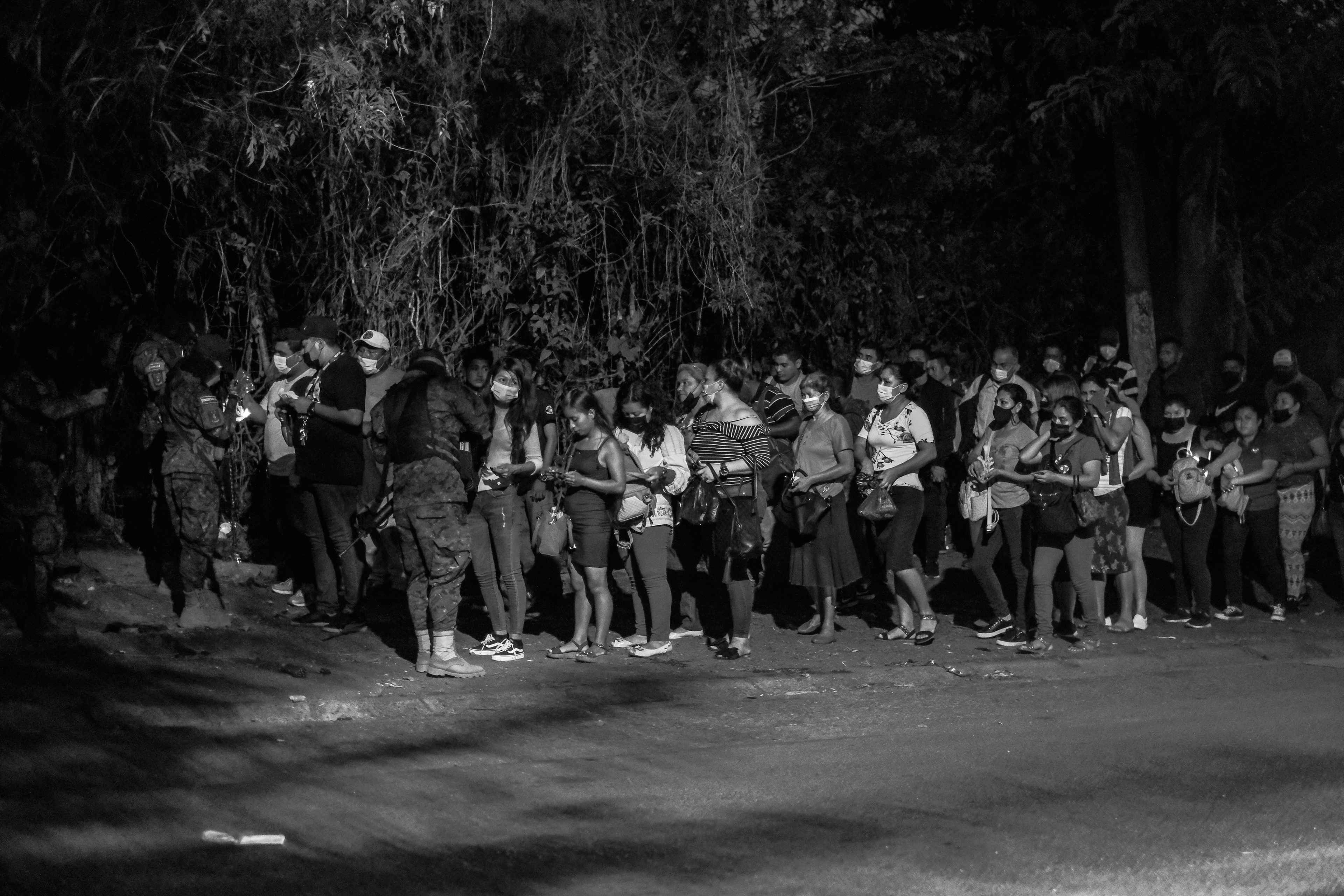 People line up to show their IDs to police at a checkpoint in Distrito Italia, San Salvador, during the first days of the state of exception in April 2022.